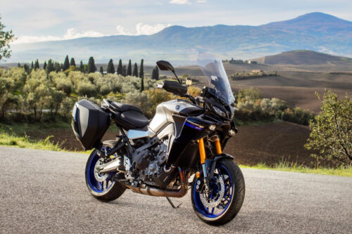 yamaha tracer 9 gt 2021 vista de ângulo frontal lateral direita, estacionada na estrada com campo e montanhas ao fundo