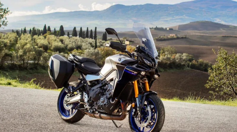 yamaha tracer 9 gt 2021 vista de ângulo frontal lateral direita, estacionada na estrada com campo e montanhas ao fundo